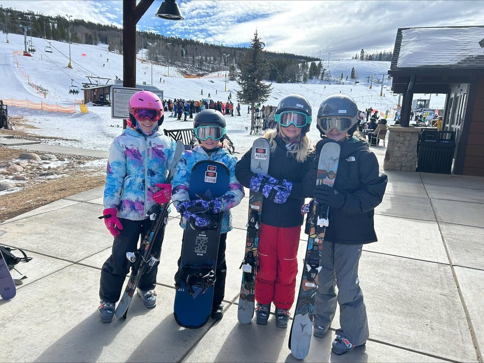 Four young riders with rental skis and snowboards at the lift base