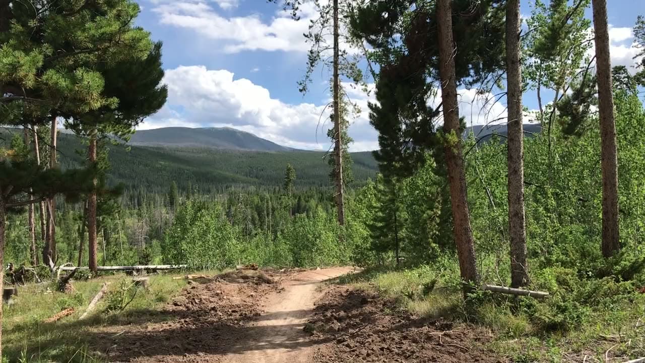 Mountain biker cresting a Winter Park trail with peaks behind